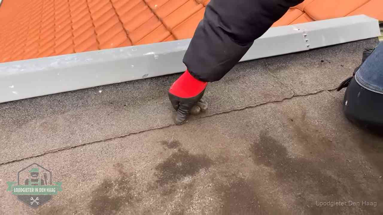 Vakman wijst een naad met vochtplekken aan op een bitumen plat dak in Den Haag