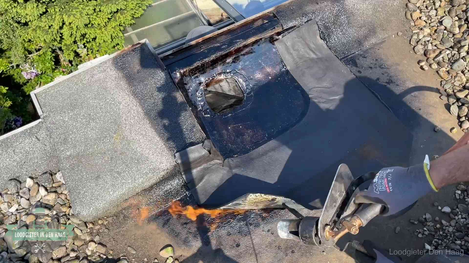Dakdekker brandt bitumen rond een doorvoer tijdens een daklekkage-reparatie in Den Haag