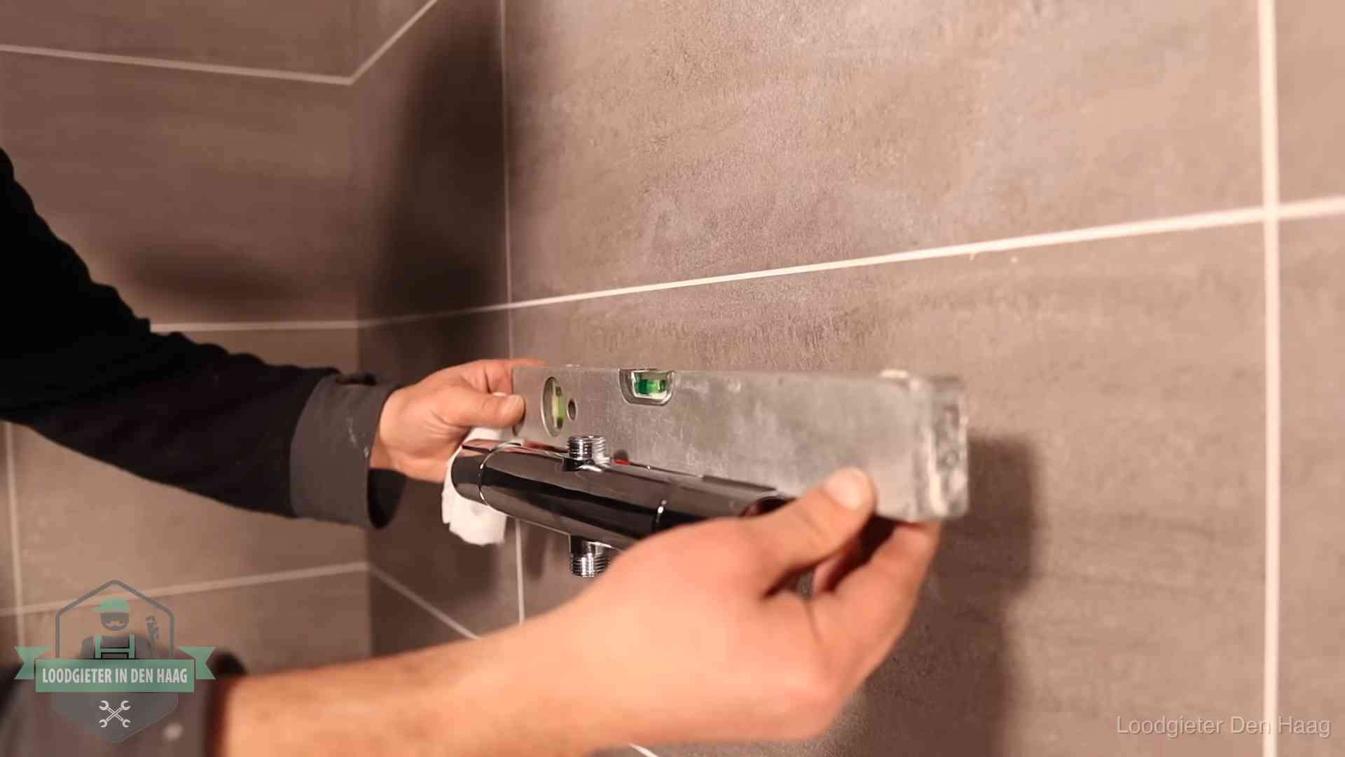 Loodgieter lijnt een douchekraan uit met een waterpas in een woning in Den Haag