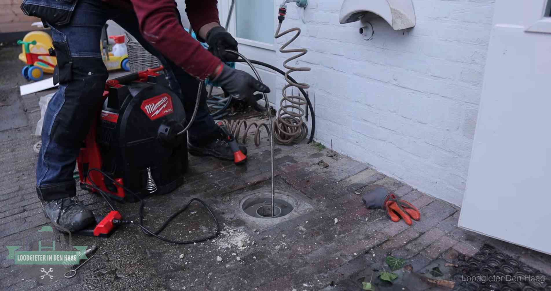 Ontstoppingsputje in de bestrating naast de gevel van een woning in Den Haag
