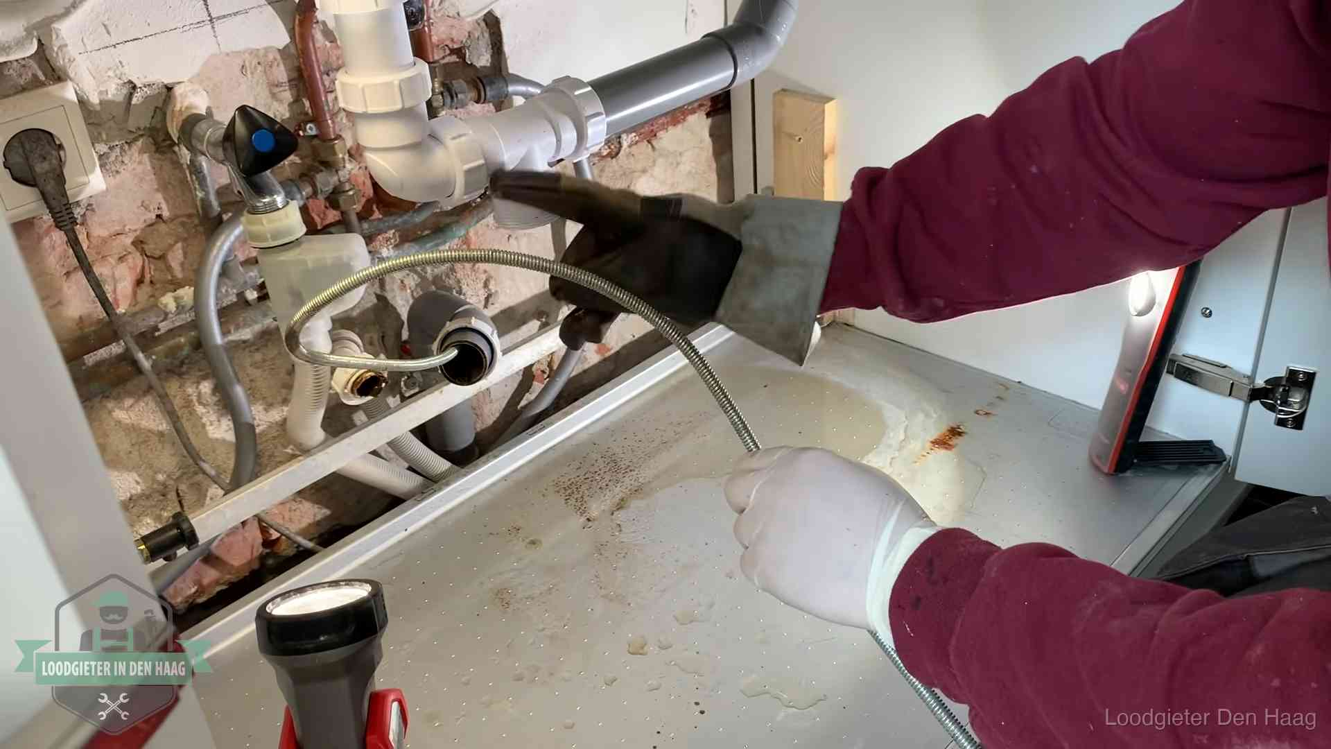 Ontstoppingsveer gaat in een geopende sifonaansluiting onder het aanrecht in Den Haag