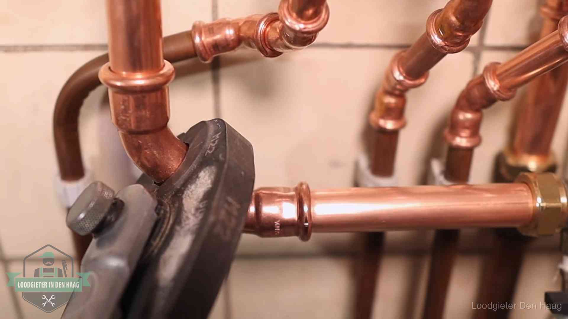 Persmachine perst een koperen fitting op nieuw leidingwerk in Den Haag