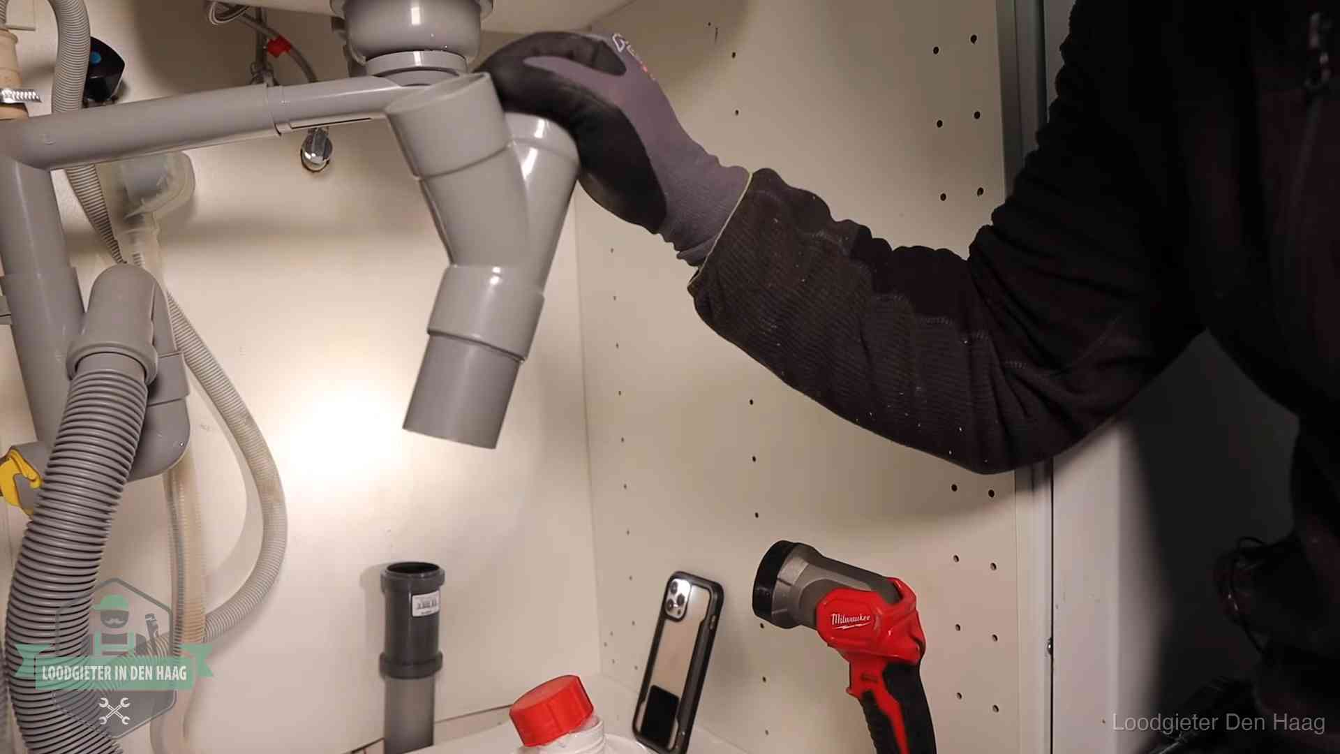 Loodgieter demonteert het sifon- en afvoerwerk onder een gootsteen in Den Haag bij stankklachten
