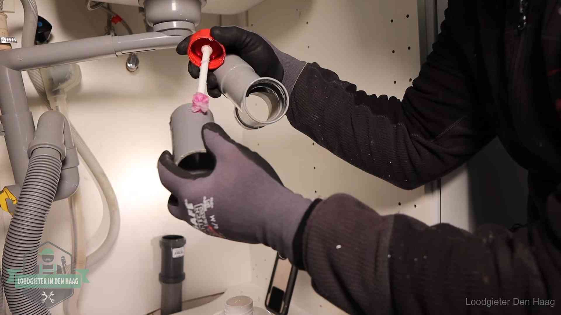 Loodgieter demonteert en reinigt de sifon onder een keukenkast in Den Haag