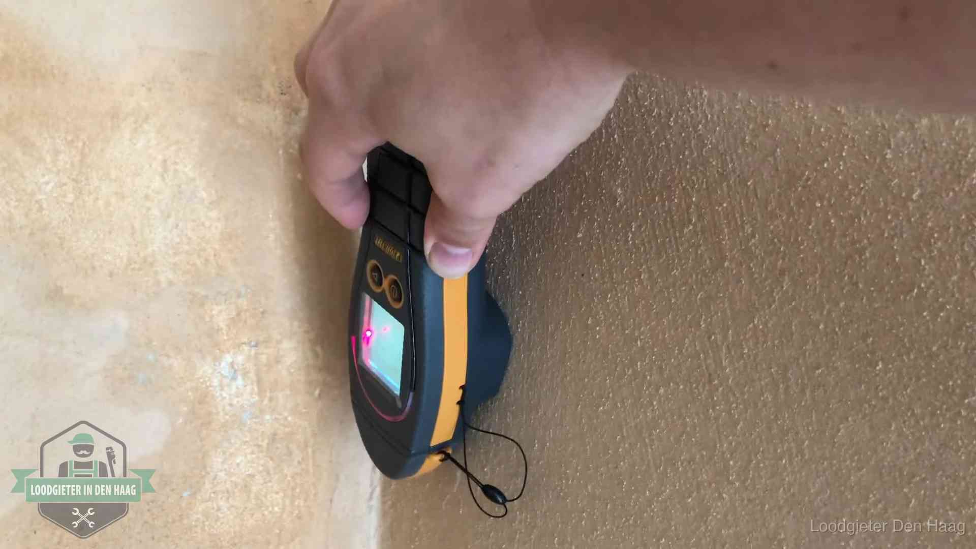 Vochtmeter tegen een muur met vochtplekken tijdens het opsporen van een daklekkage in Den Haag