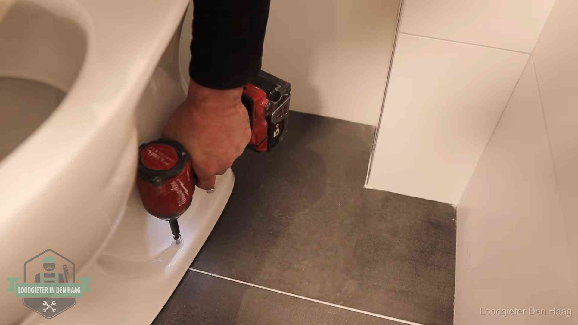 Loodgieter zet de voet van een wc-pot vast op de tegelvloer in Den Haag